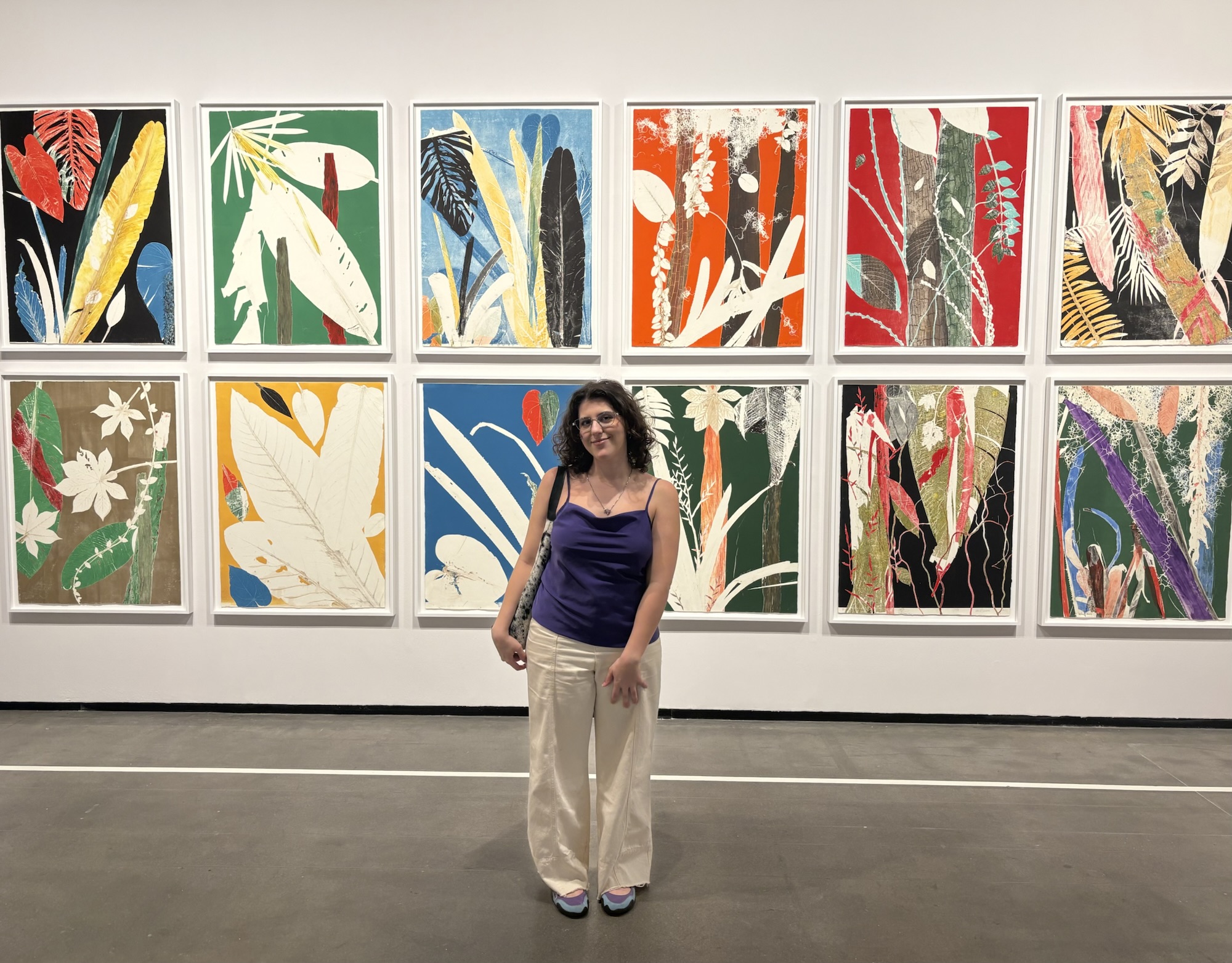 Eu na frente de uma parede de galeria, cheia de gravuras de Luiz Zerbini